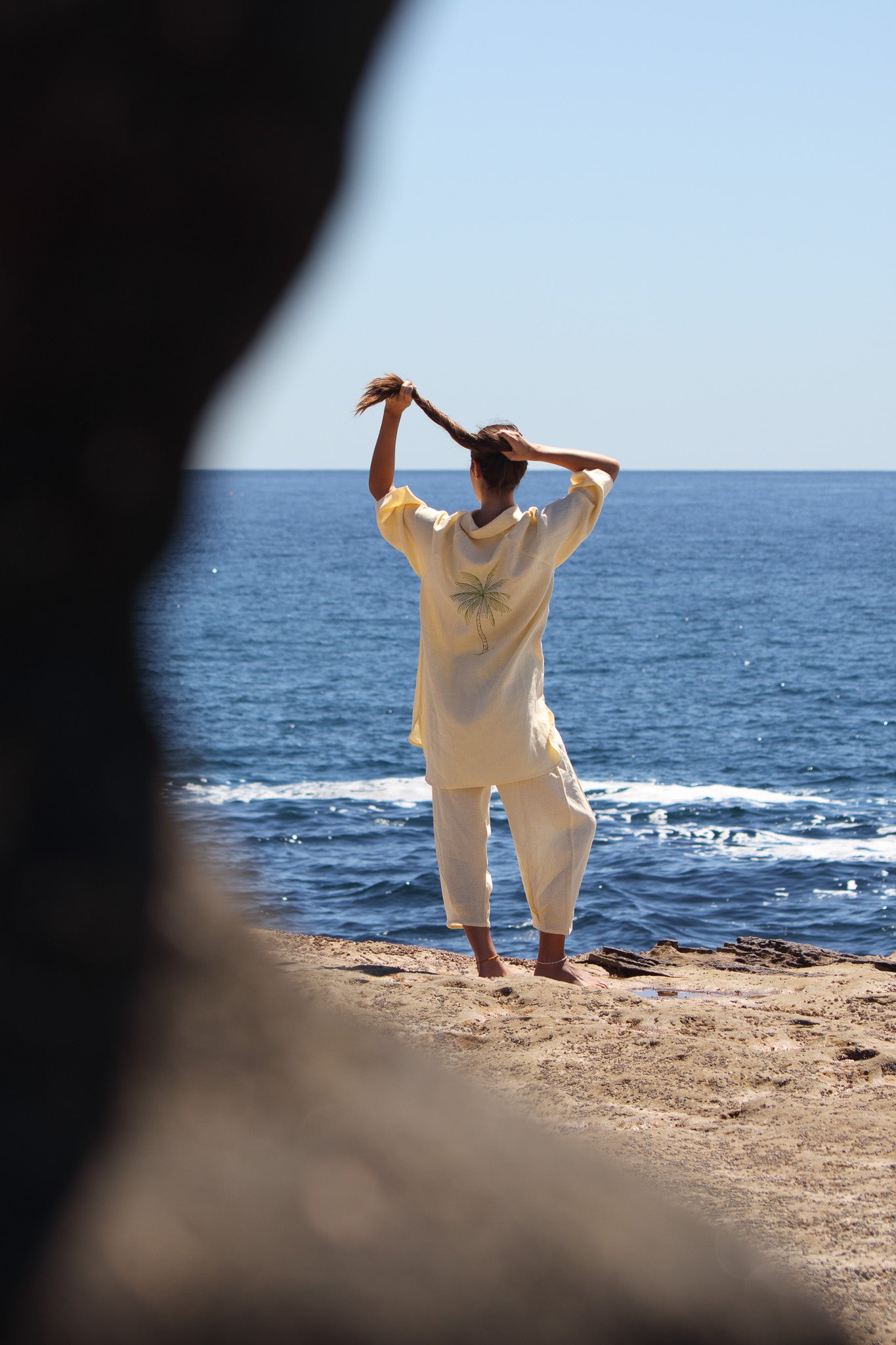 Butter yellow Oceanic Shirt Dress with palm tree embroidery on the back worn by the water.
