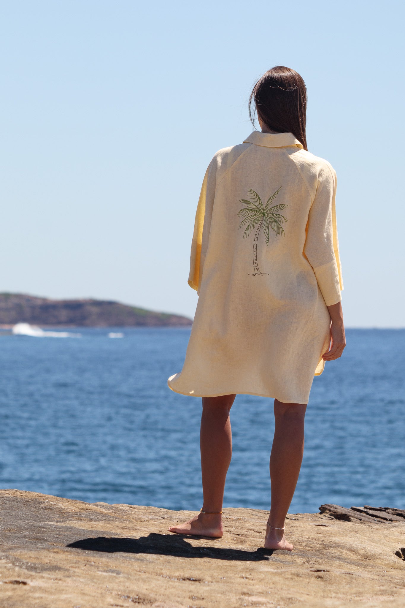 Back view of the butter yellow Oceanic Shirt Dress showing the palm tree detail and curved hem.