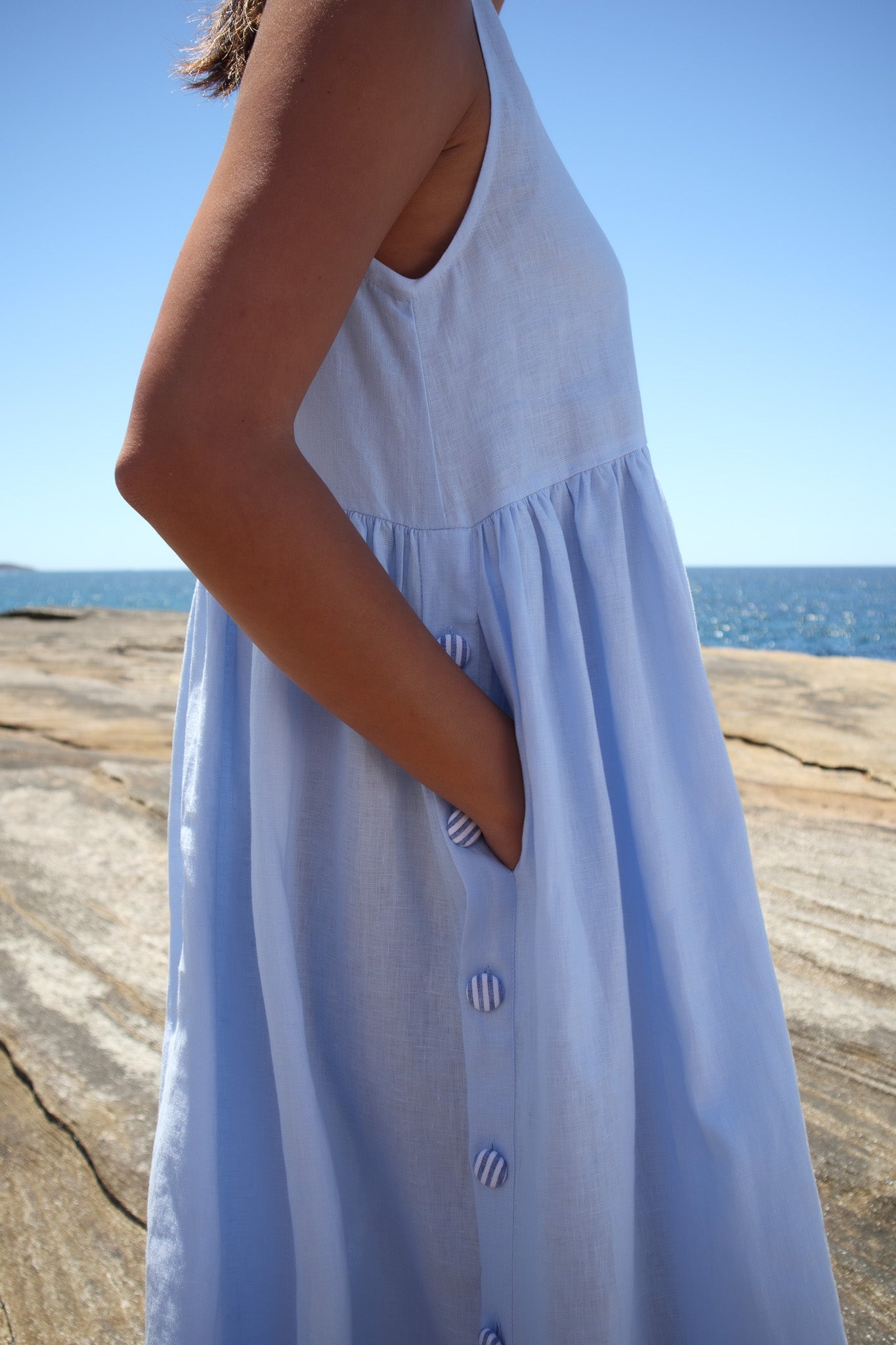 Side detail of the Wonka Dress in sky blue linen, showing the striped covered buttons and hidden pocket.