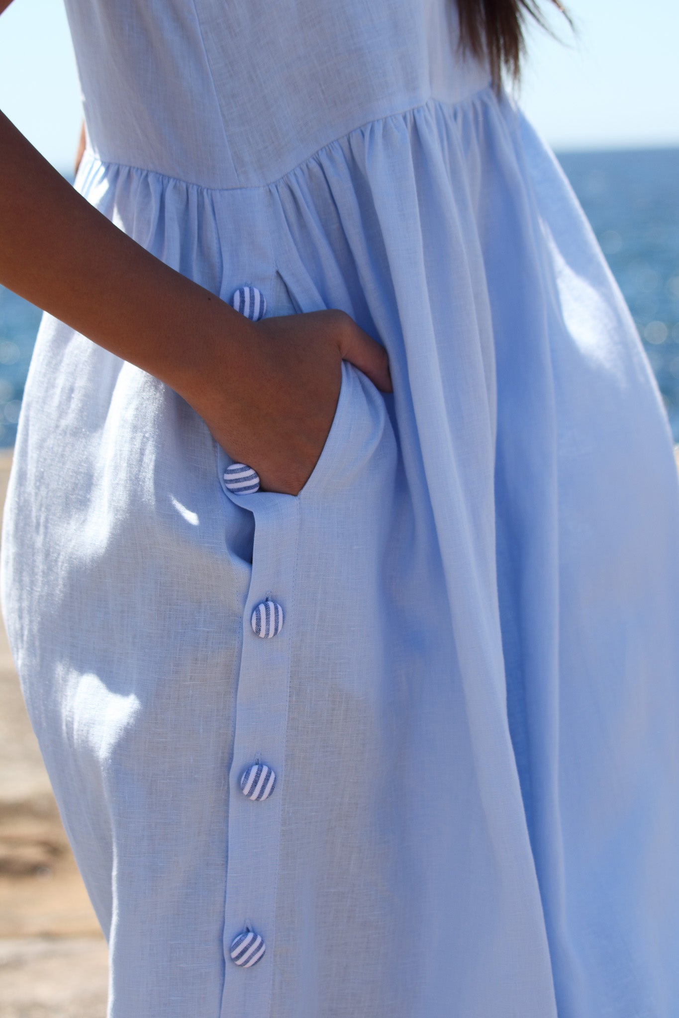 Close up of the Wonka Dress in sky blue linen, showing the side pocket and striped covered buttons.