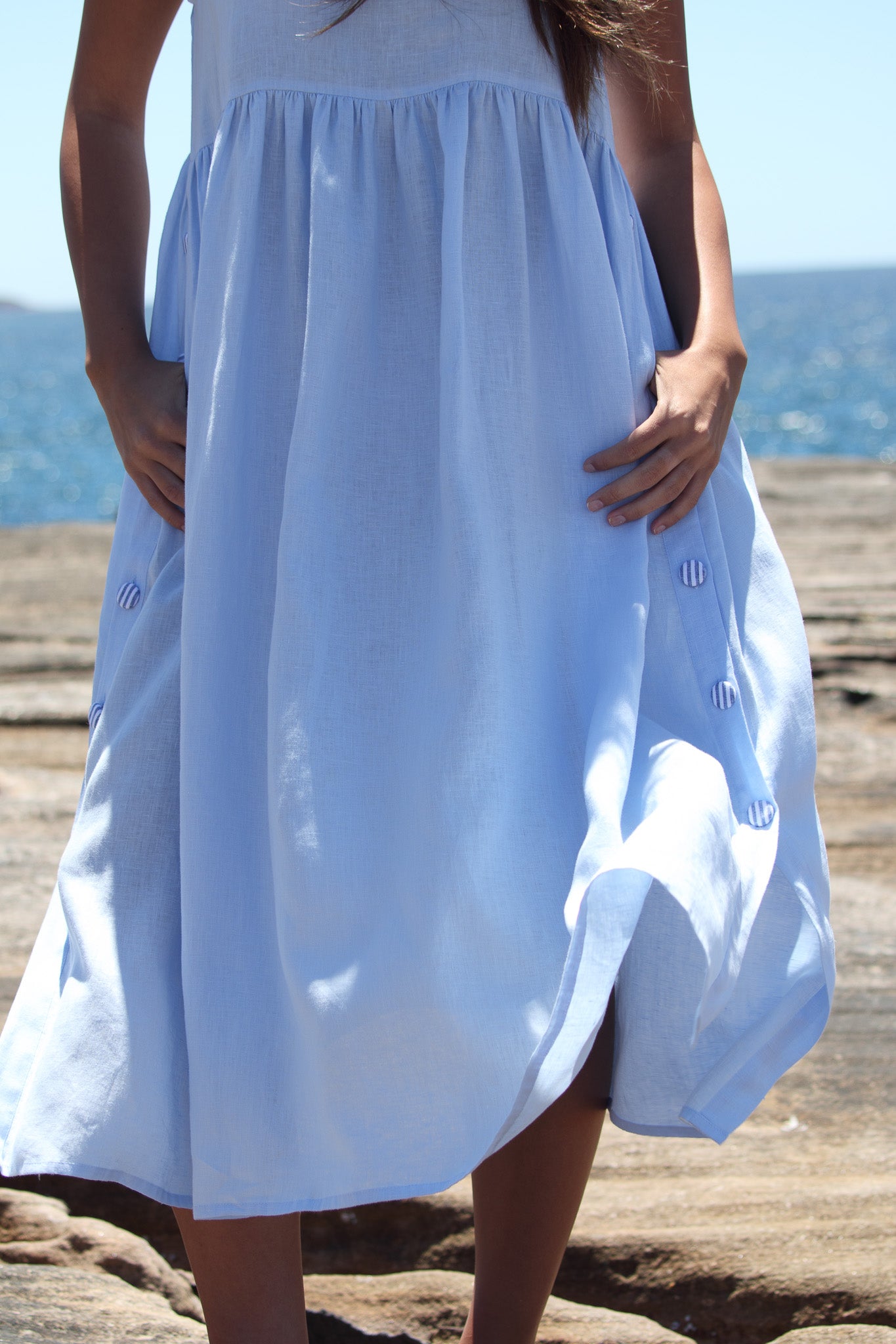 Close up of the Wonka Dress in sky blue linen, showing the side split, striped covered buttons and soft movement.