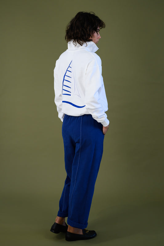 Back view of white cotton jumper with blue embroidered sailboat shown full length