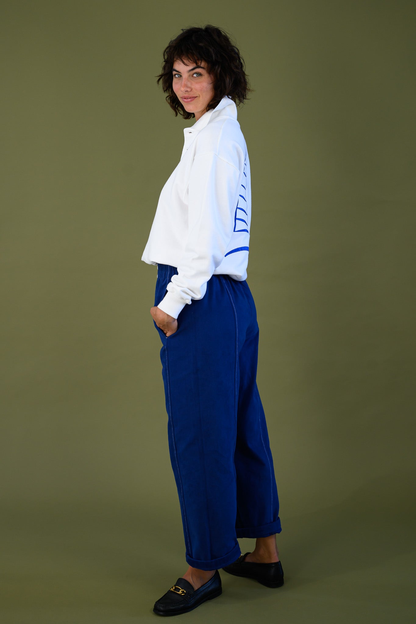 Side view of white cotton jumper styled with blue pants shown full length on model
