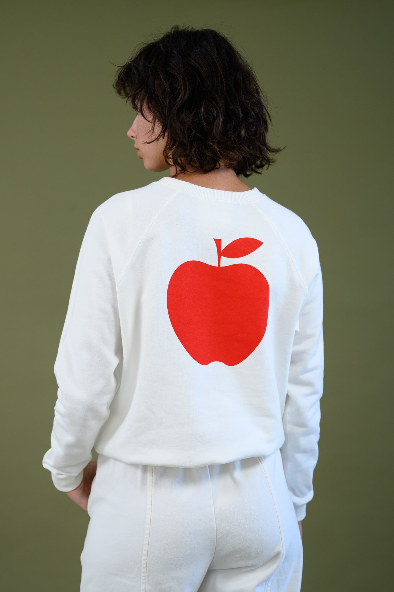 Angled back view of white cotton sweatshirt highlighting apple graphic