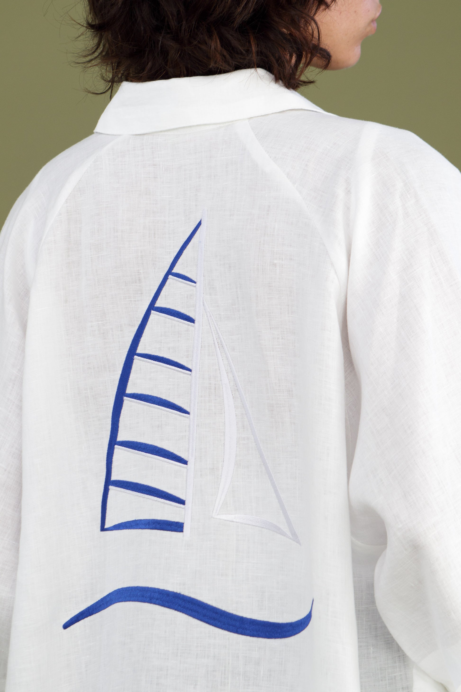 Close up of white linen shirt dress showing blue embroidered sailboat on back