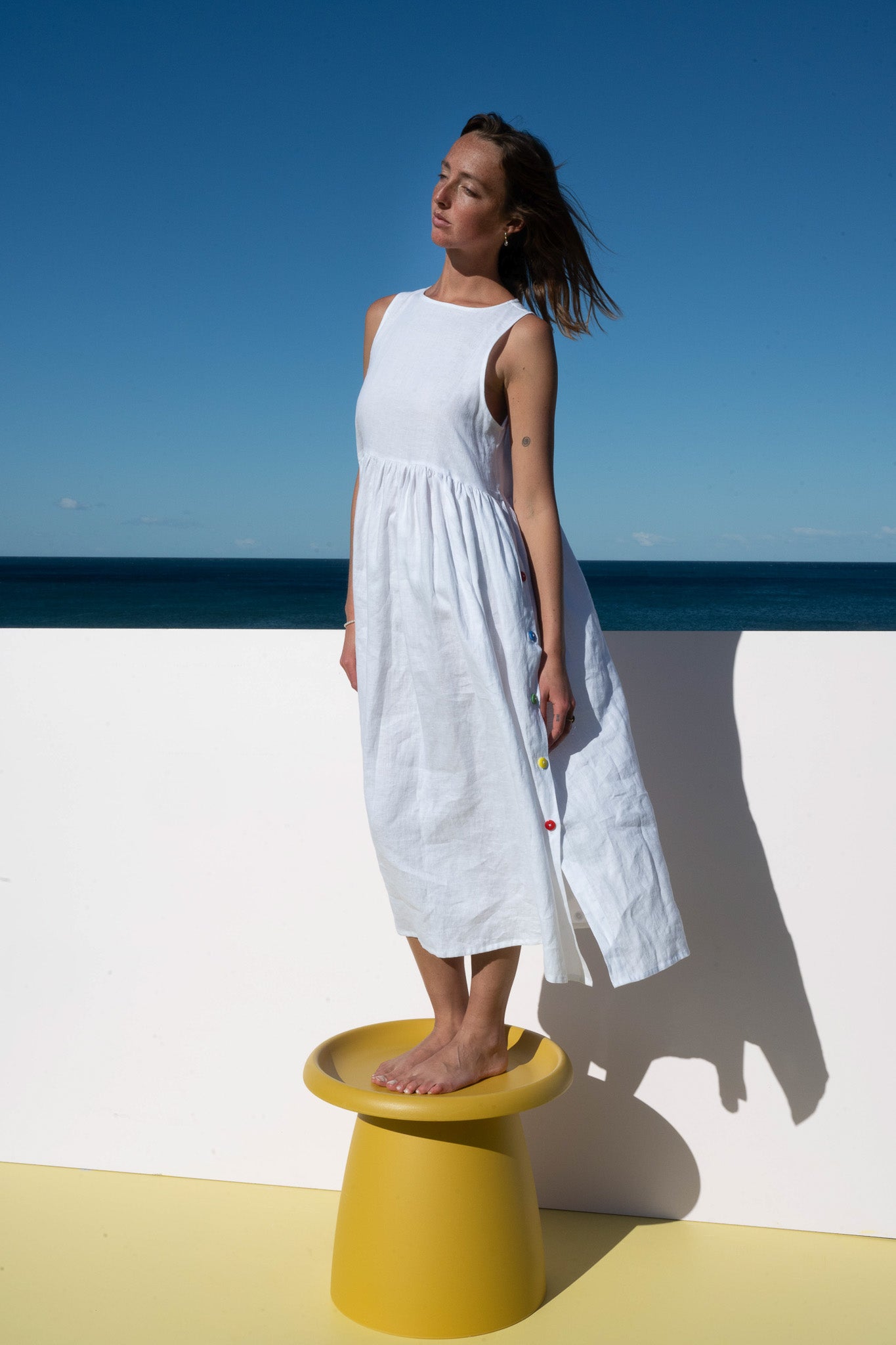 Full-length view of the Wonka Sleeveless Dress in crisp white linen with rainbow button accents.