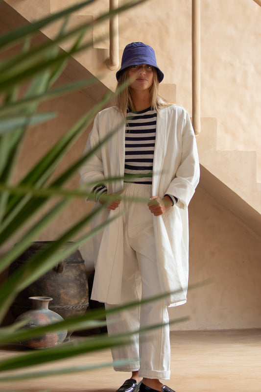 Yoko Kimono Coat in Vanilla styled with striped top and white trousers, captured through foliage for a lifestyle vibe.